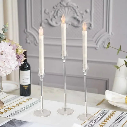 The elegant dining table features three tall, white LED candles from candletown.net in sleek acrylic holders. A wine bottle and floral vase adorn the table with a patterned runner and napkins, completing the modern look against ornate wall paneling in the backdrop.