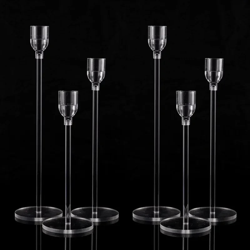 A set of six clear acrylic candle holders from candletown.net, displayed on a black background, features varying heights with circular bases and elongated stems. These modern pieces are designed to enhance your decor with their cup-like tops, ideal for holding candles.